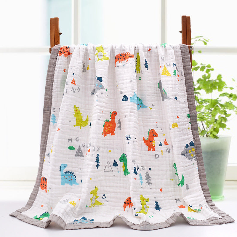 A colorful baby blanket with cartoon dinosaurs in red, green, yellow, and blue on a white background with a gray border. The blanket is draped over a wooden rack indoors.