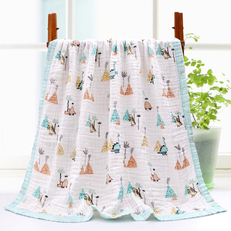 A white quilt with a turquoise border featuring colorful dinosaur illustrations is draped over a wooden rack. A potted plant is visible in the background near a window.
