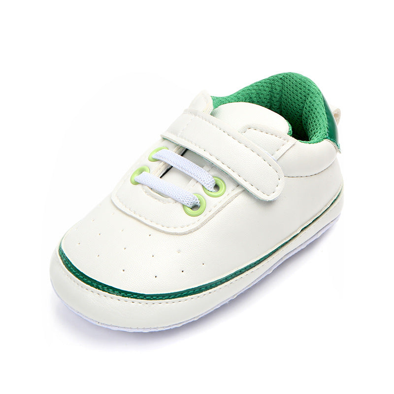 White baby shoe with a green interior and accents, featuring a hook-and-loop strap, white laces, and green eyelets. Simple design with a soft sole for infants.