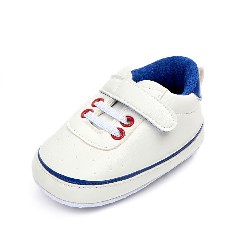 White infant shoe with blue accents and red lace eyelets. It features a single Velcro strap for fastening and a soft blue lining, designed for comfort and easy wear.