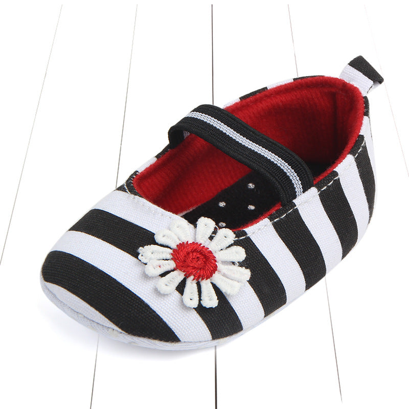 Black and white striped baby shoe with red interior and a white flower embellishment on top. The shoe has a black strap and is placed on a white surface.