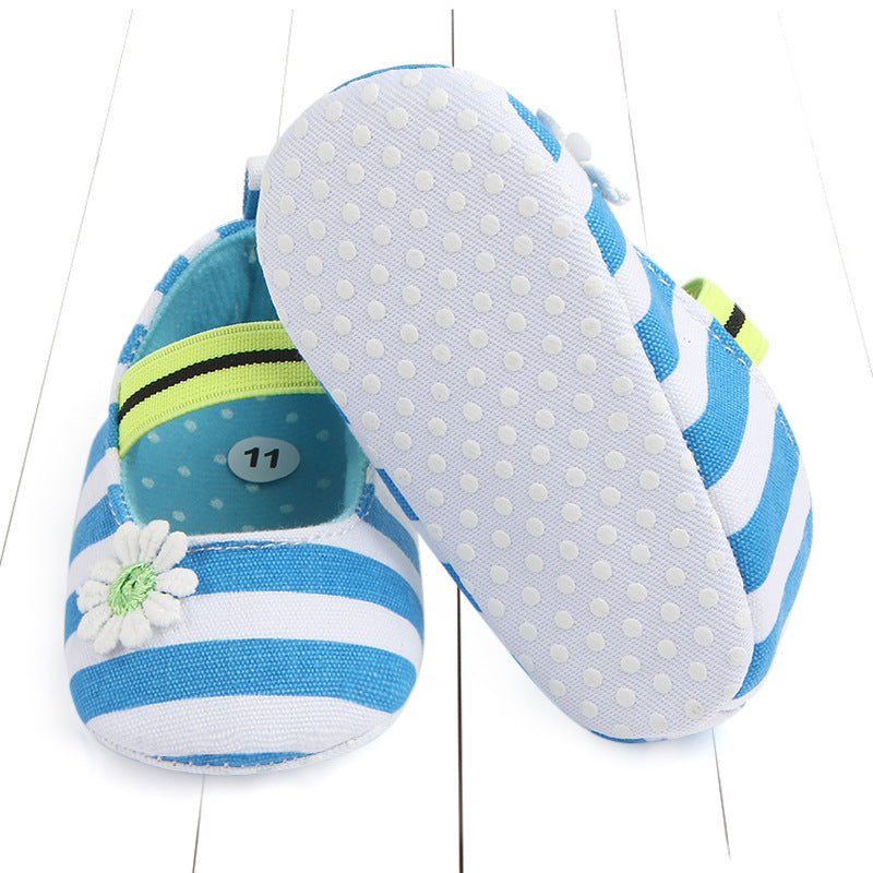 Blue and white striped baby shoes, one showing a daisy flower decoration, and the other revealing a non-slip white sole with tiny dots. A size label with the number 11 is inside.