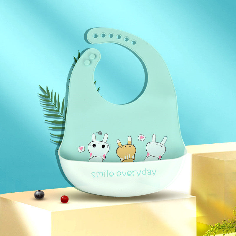 Light blue baby bib with cartoon animals and "smile everyday" text hangs in front of a blue background. A fern and colored beads decorate the scene.