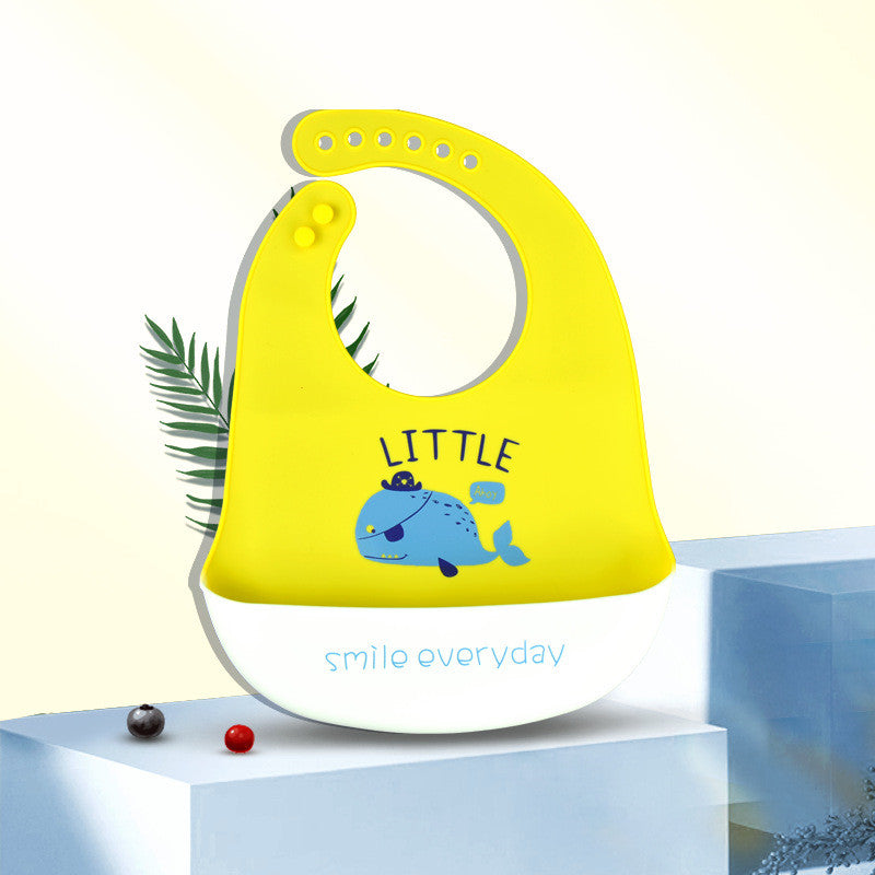 Bright yellow baby bib with a blue whale design and the words "LITTLE" and "smile everyday." It features adjustable buttons and rests on a white surface with decorative leaves.