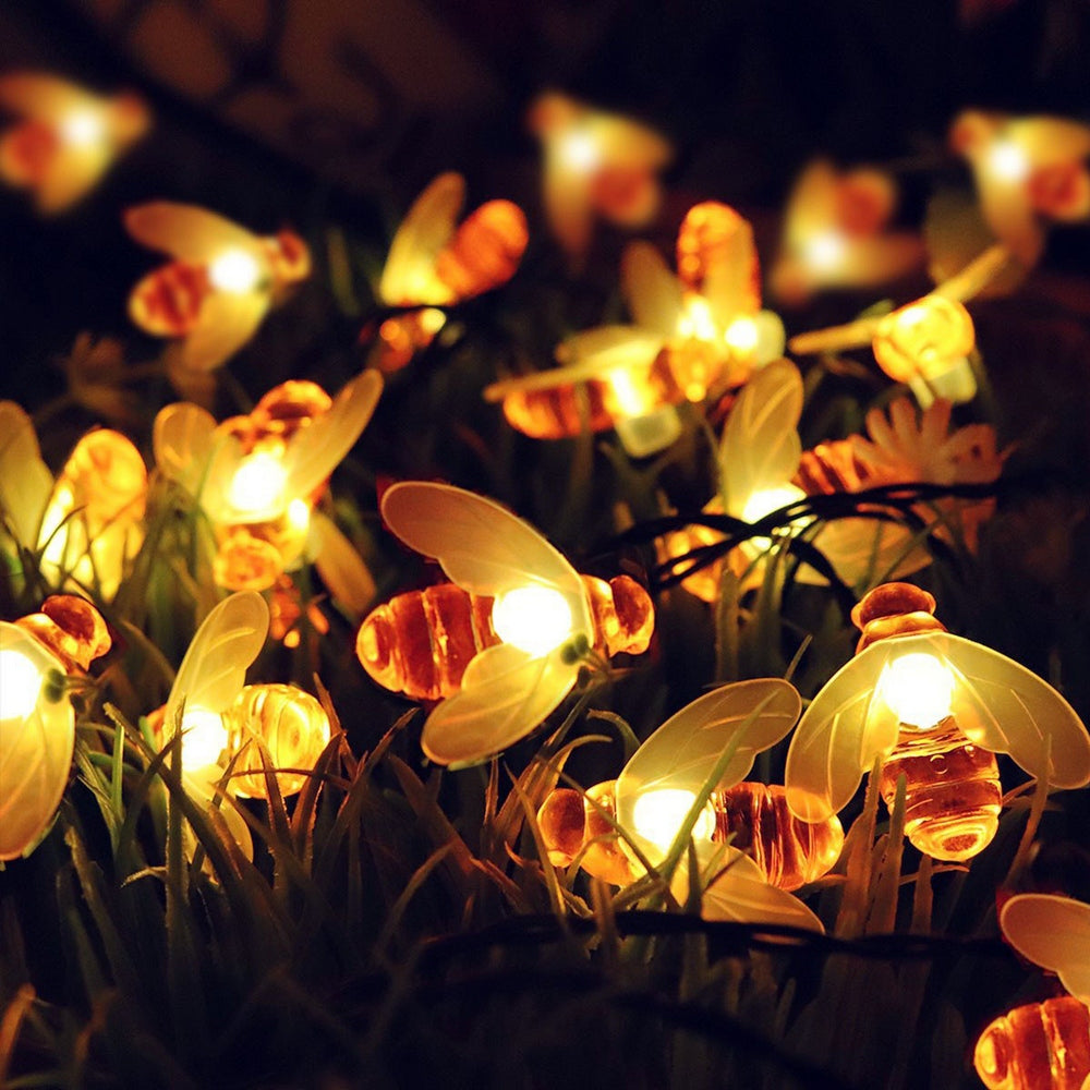 Glowing bee-shaped fairy lights are nestled among blades of grass, emitting a warm, cozy ambiance in the dark.