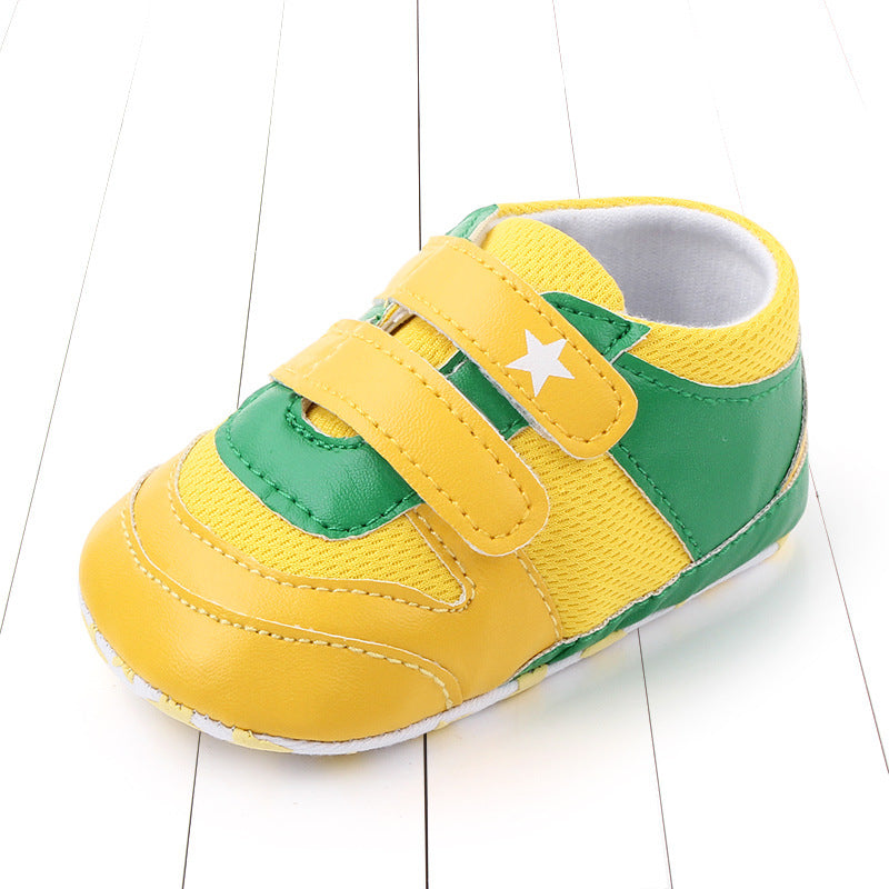Yellow and green baby sneaker with Velcro straps and a white star on the side, set on a white wooden floor.