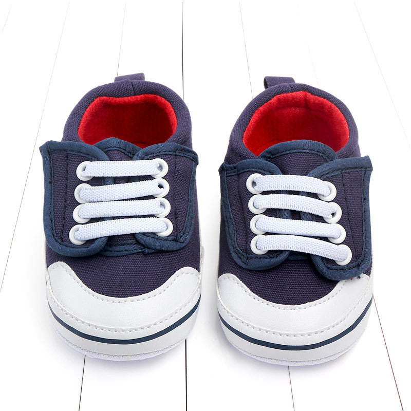 Navy blue baby sneakers with white and navy toe caps, white laces, and red interior, placed on a white wooden surface.