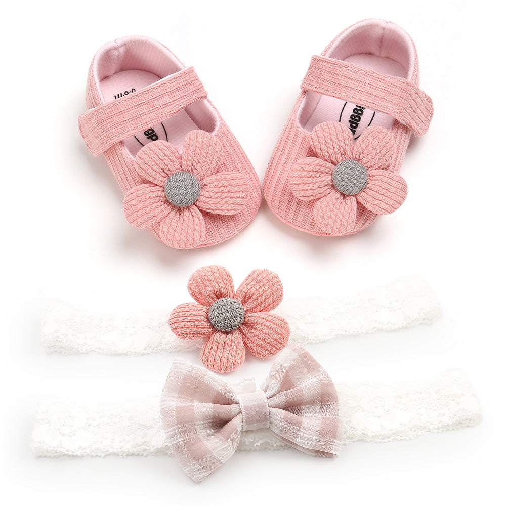 Pink baby shoes with flower accents and two lace headbands, one with a pink flower and the other with a plaid bow, arranged on a white background.