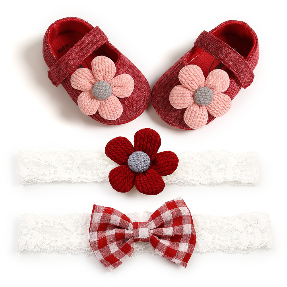 Red baby shoes with pink flower embellishments, paired with a white lace headband featuring a red flower, and another with a red checkered bow.