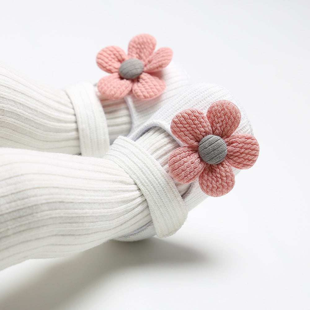 Baby wearing white ribbed socks and pink flower booties with gray centers on a white background.