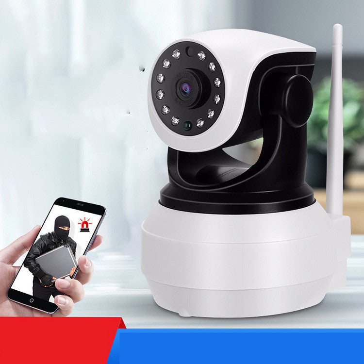 A white and black security camera with LED lights stands on a surface, while a hand holds a smartphone displaying an intruder alert in the background.