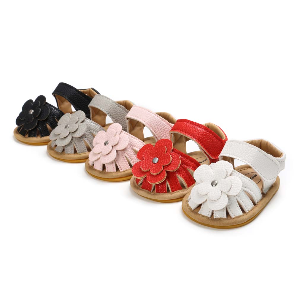 Five pairs of baby sandals in black, gray, pink, red, and white, each adorned with a flower embellishment, are lined up diagonally on a white background.