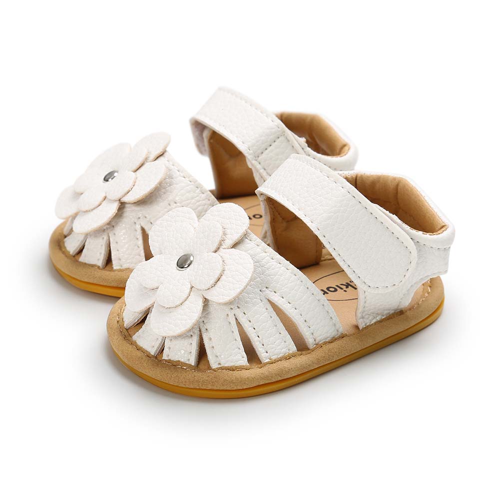 White baby sandals with velcro straps and flower decorations on the front. The sandals have a tan sole and are designed for comfort and style.