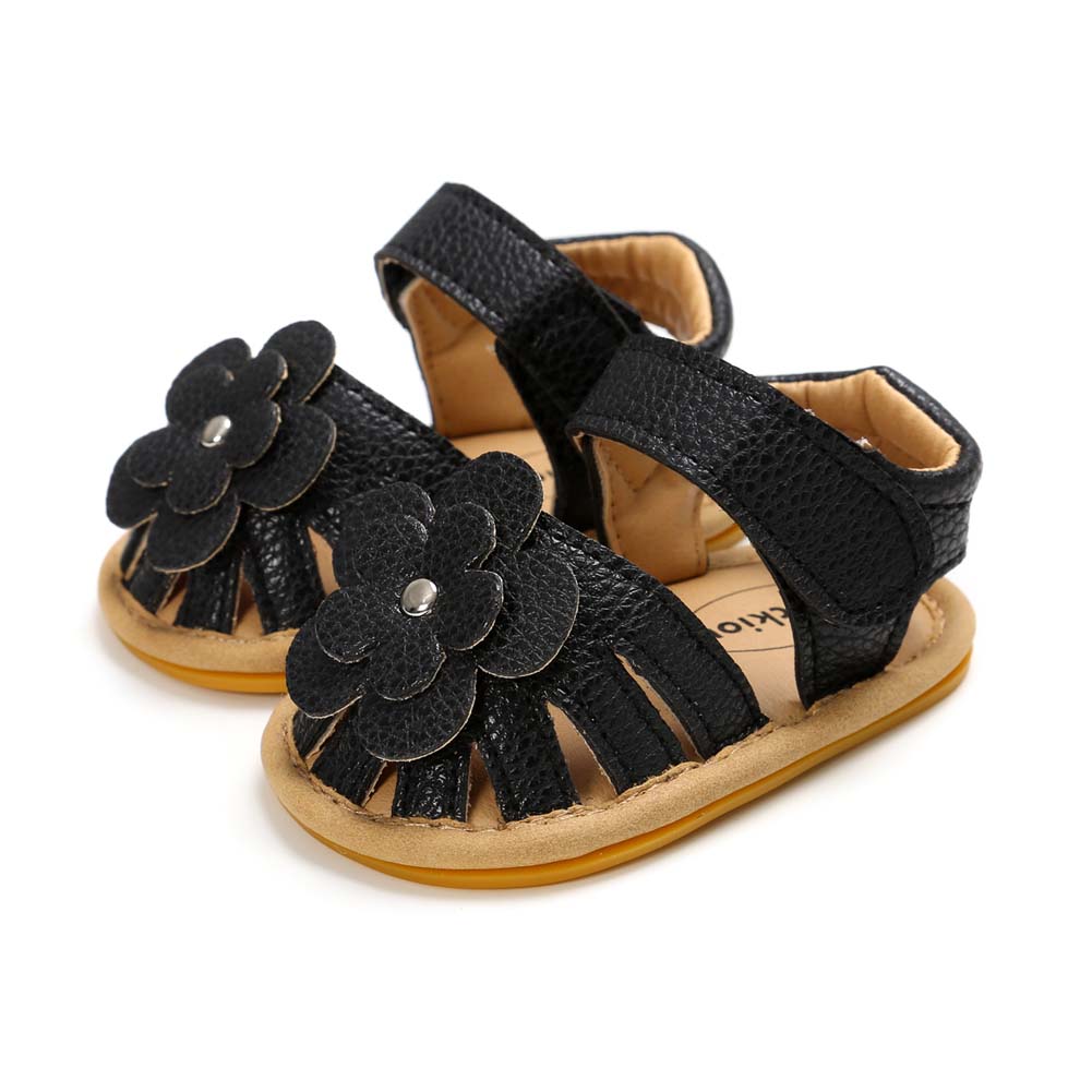 Black toddler sandals with flower decorations and open toes. The sandals have a pebbled texture and light brown soles, featuring adjustable ankle straps.