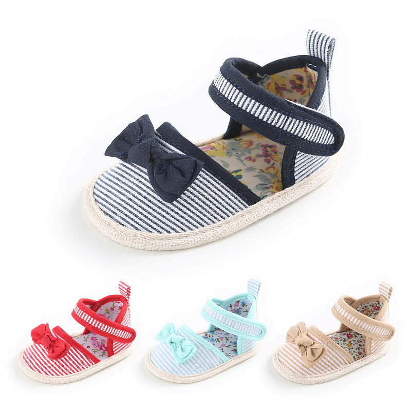 Striped baby shoes in navy, red, light blue, and beige, each featuring a bow on the front and a floral interior. The design includes Velcro straps and soft soles.