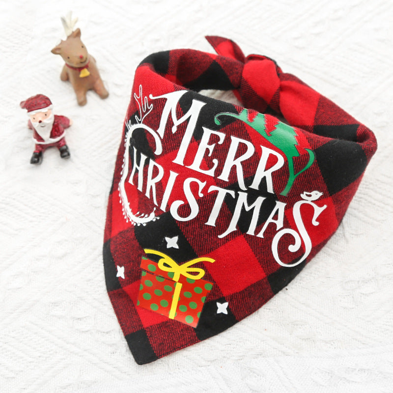 Red plaid bandana with "Merry Christmas" text, green tree, and yellow gift design. Small Santa figure and reindeer toy are placed on a white textured surface nearby.