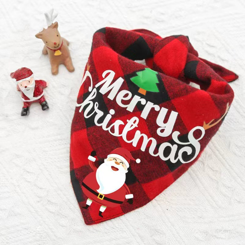 Red and black plaid Christmas pet bandana with "Merry Christmas" text and Santa graphic, placed on a white surface. Nearby are small figurines of Santa and a reindeer.