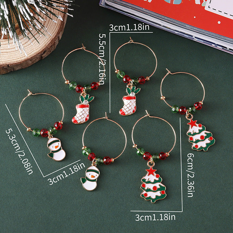 Six festive wine glass charms with Christmas designs, including snowmen, stockings, and trees, are shown. Each charm measures 3cm in diameter. Decorations are red and green beads.