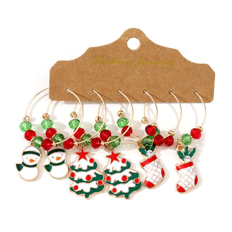 Festive wine glass charms featuring snowmen, Christmas trees, and stockings with red and green beads, displayed on a brown card labeled "Fashion Jewelry".