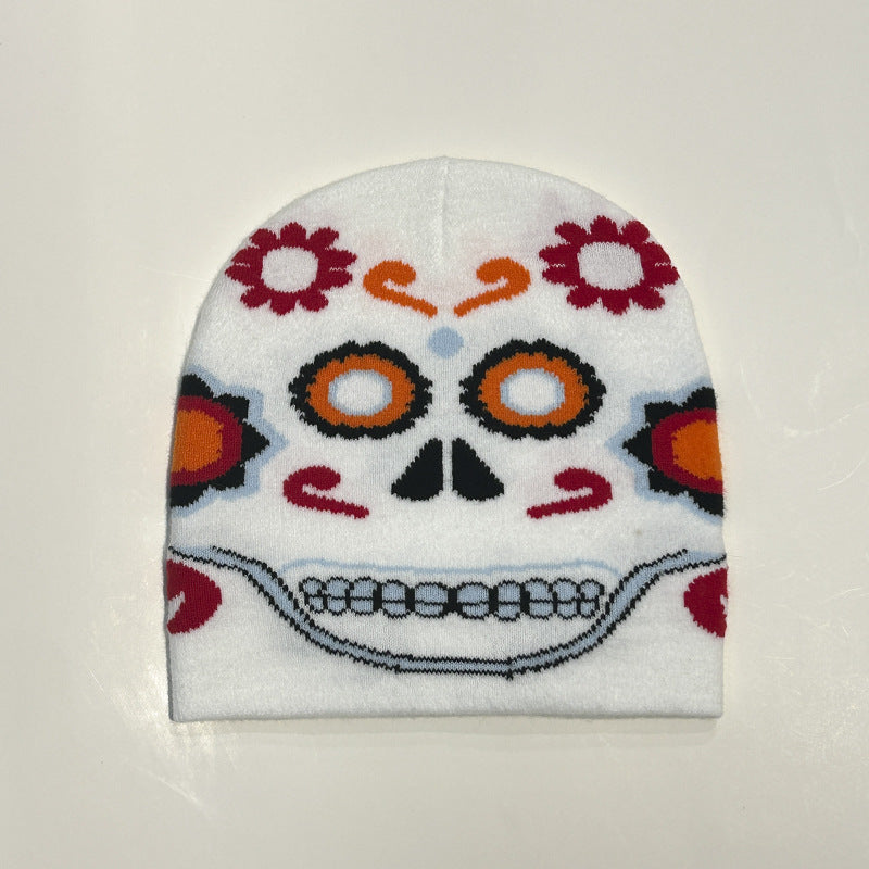 White beanie with a colorful sugar skull design featuring orange and red floral patterns, stylized eyes, a triangular nose, and a wide smile on a plain background.