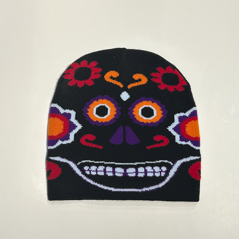 Black beanie with a colorful Day of the Dead inspired design featuring orange and purple eyes, floral patterns, and a vibrant skull motif on a neutral background.