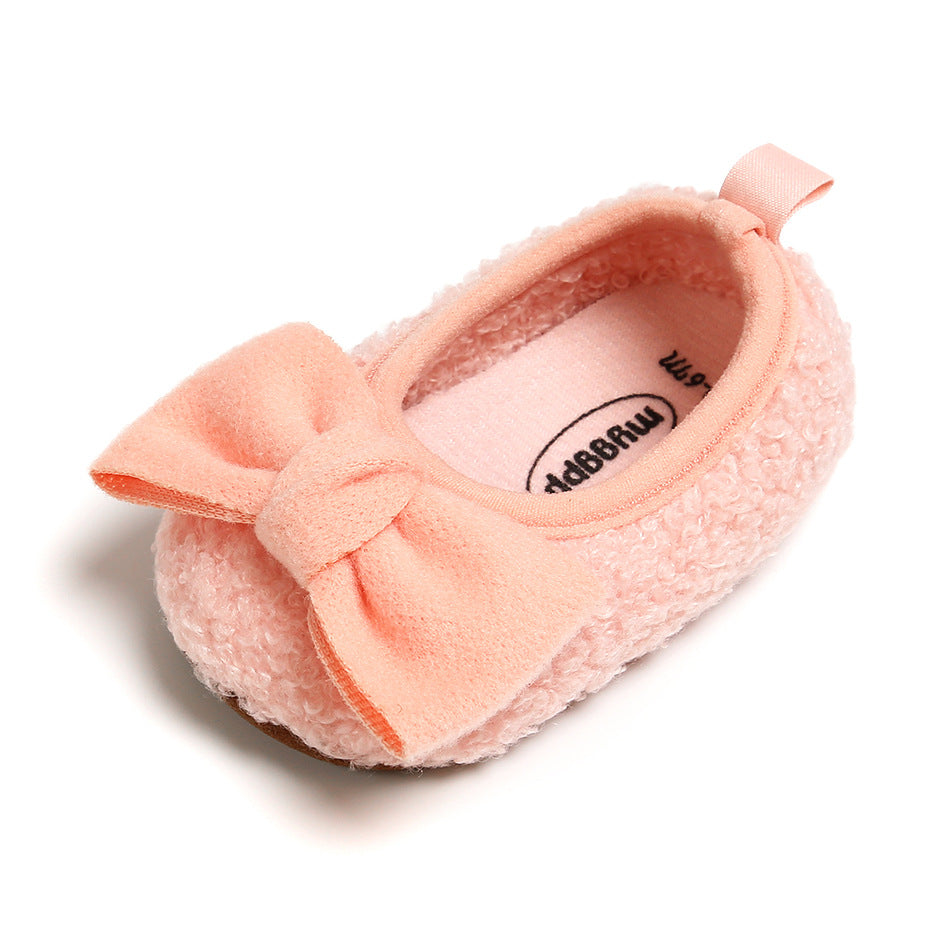 Soft pink baby shoe with a textured, fluffy exterior and a matching bow. The interior is lined with a smooth fabric. Suitable for infants or toddlers. Elegant and cozy design.