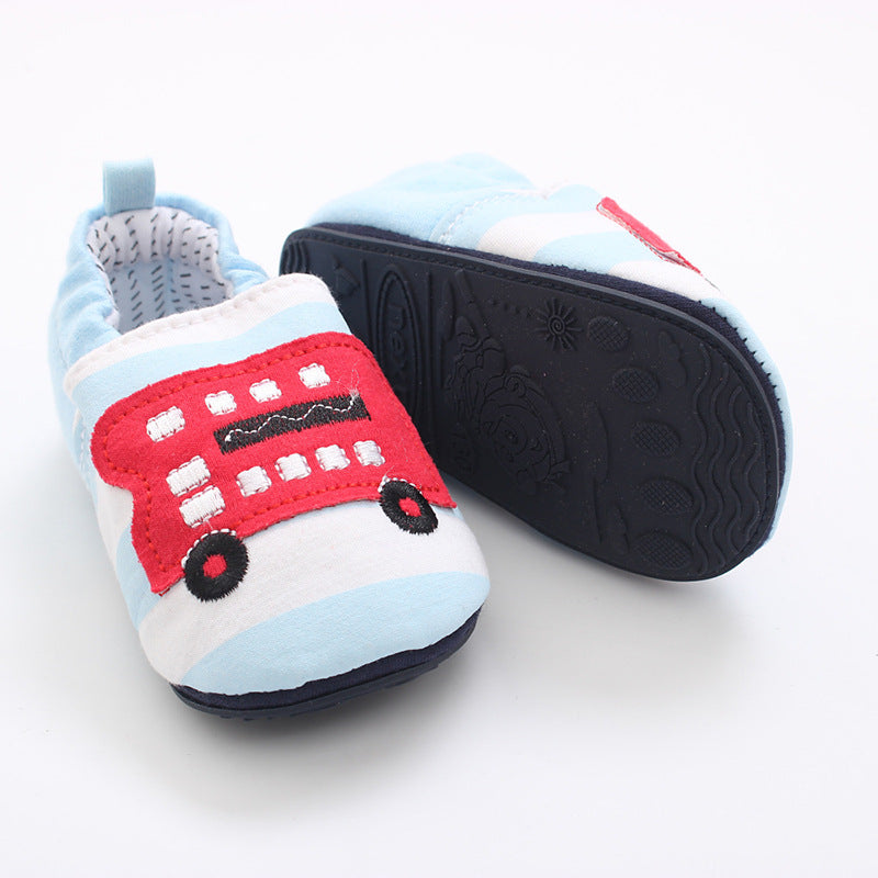 Light blue baby shoes with soft soles, featuring an embroidered red double-decker bus design and non-slip bottoms. Displayed with one shoe top and the other sole up.