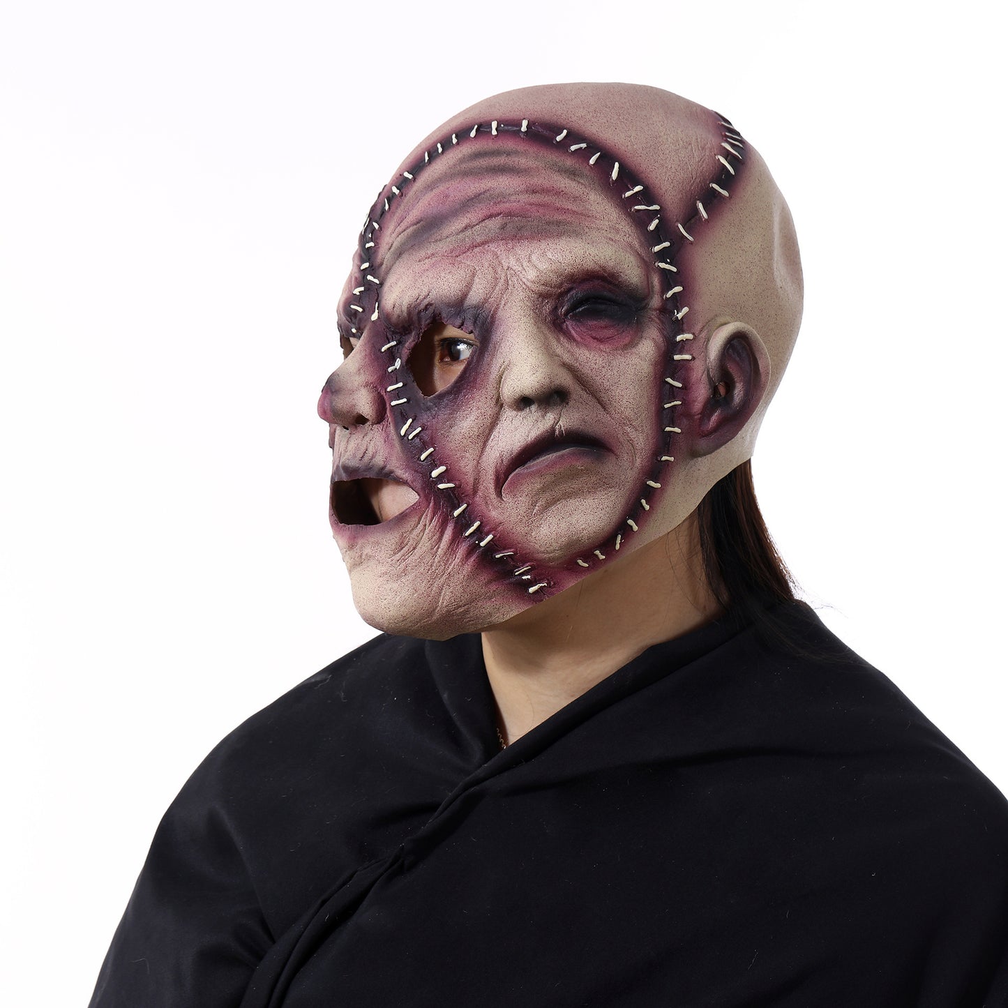 A person wearing a detailed, grotesque mask resembling stitched, torn skin with exaggerated facial features. The mask is worn over a black cloak, creating a spooky appearance.