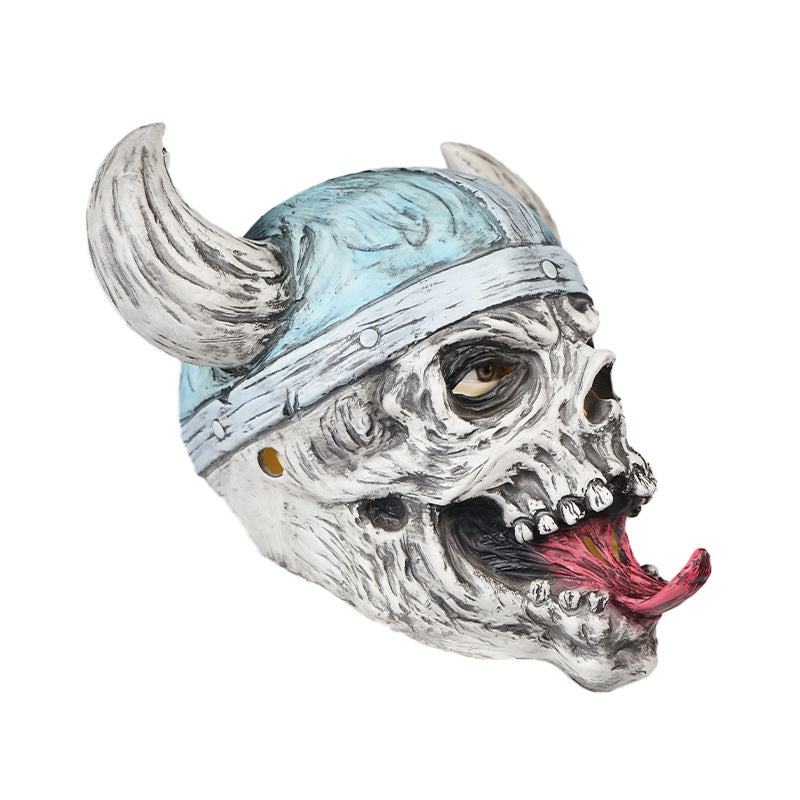 A grotesque skull mask with an open mouth and protruding tongue, featuring a blue Viking helmet with curved horns. The mask has a detailed, textured surface and hollow eyes.