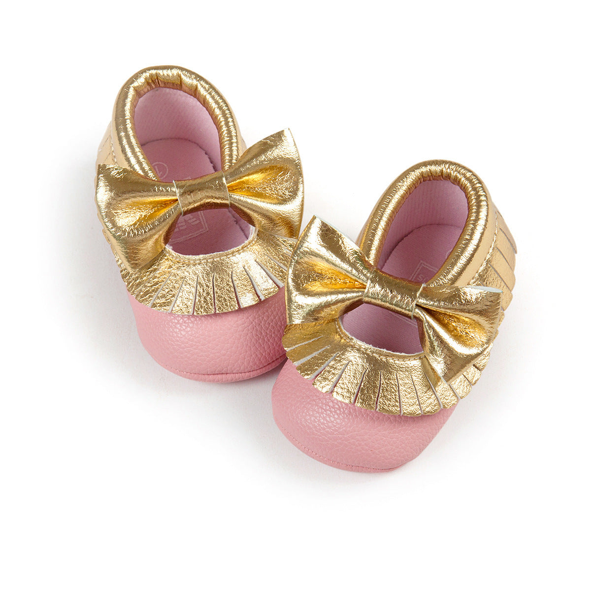 Pink baby shoes with large gold bows and fringe detail on the front. The shoes have a shiny gold trim and soft texture, designed for infants or young toddlers.