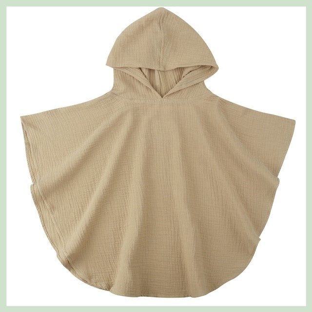 Beige hooded poncho made of textured fabric, displayed against a light background. The poncho features wide arm openings and a soft drape, offering a casual and comfortable style.