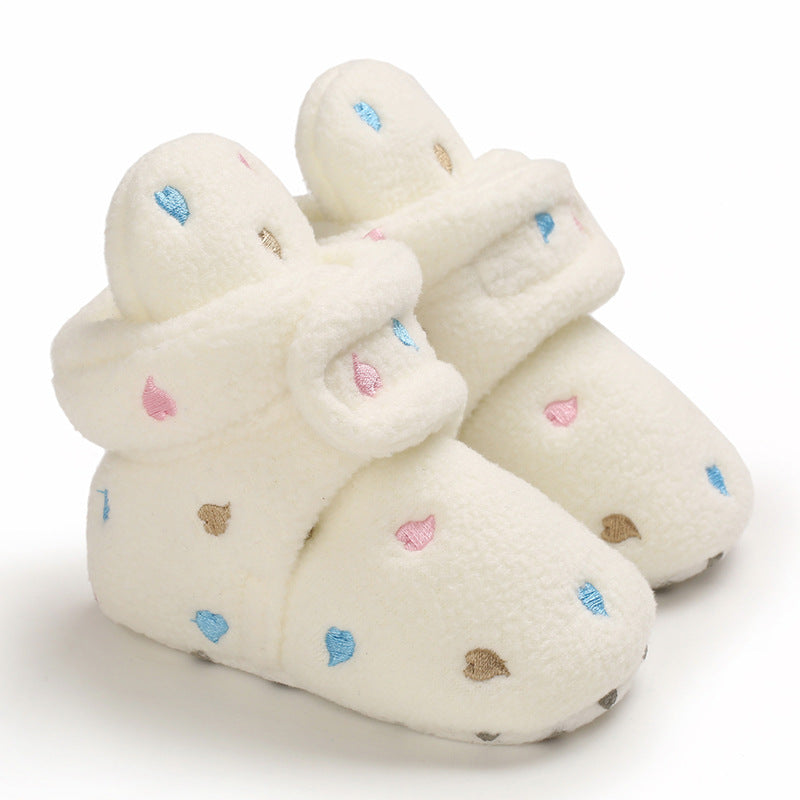 Cream-colored baby booties adorned with pink, blue, and brown embroidered hearts, featuring a soft fleece texture and a fold-over design for added warmth and snug fit.