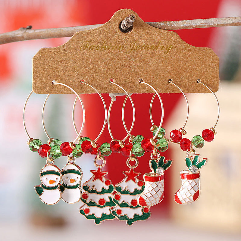 Set of festive wine glass charms featuring snowmen, Christmas trees, and stockings. Each charm is adorned with red and green beads, hanging from a cardboard display labeled "Fashion Jewelry."