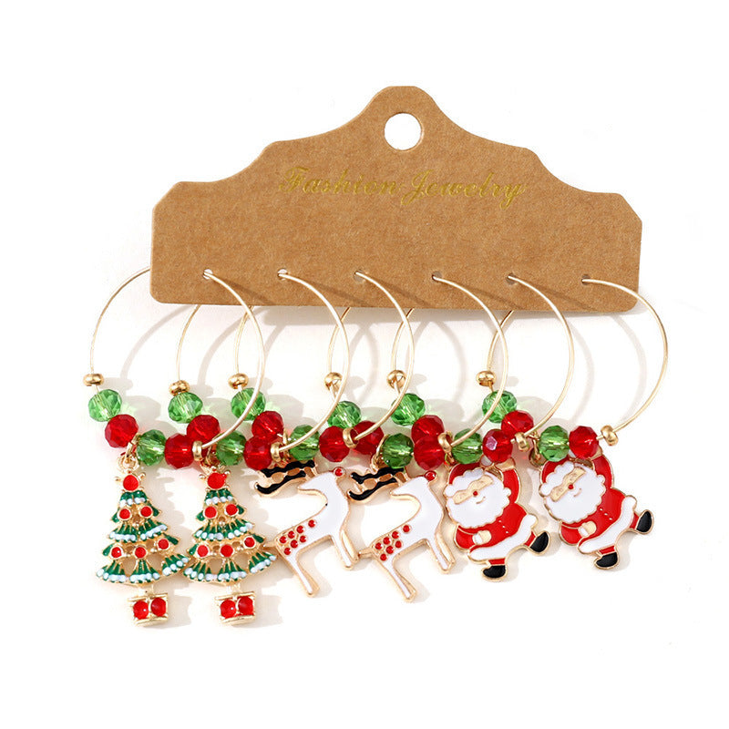Set of six wine glass charms with festive designs, including Christmas trees, reindeer, and Santa. Each charm is adorned with red and green beads, on a golden hoop.