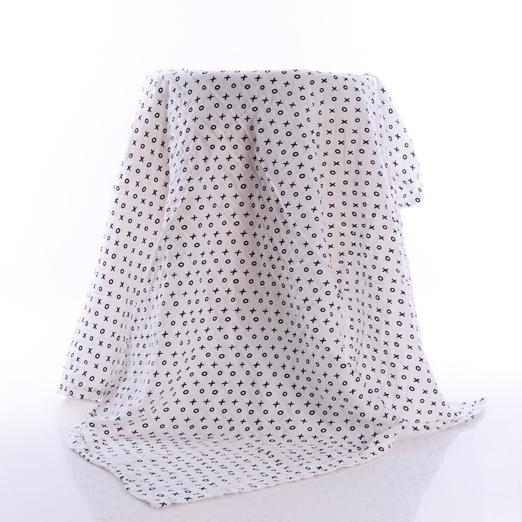 White fabric draped over a surface, with a pattern of black X's and O's. The fabric is folded and extends onto the floor, creating soft shadows on a white background.