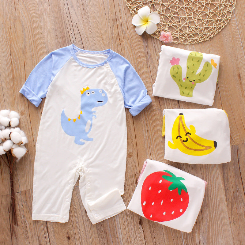 Baby romper with blue dinosaur design, surrounded by folded onesies featuring cactus, banana, and strawberry prints, placed on a wooden floor with cotton and flowers.