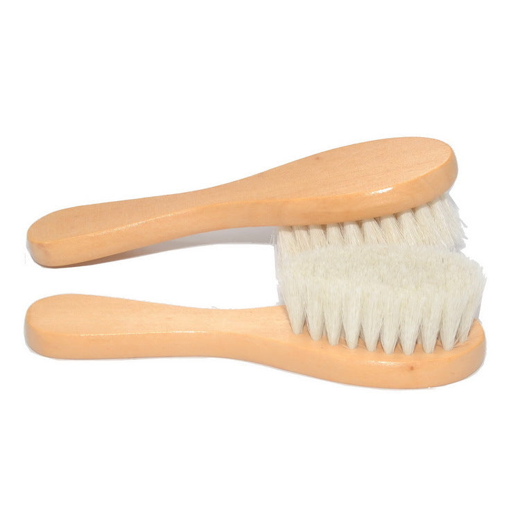 Two wooden baby hairbrushes with soft white bristles are placed against a white background, overlapping slightly to form an X shape.