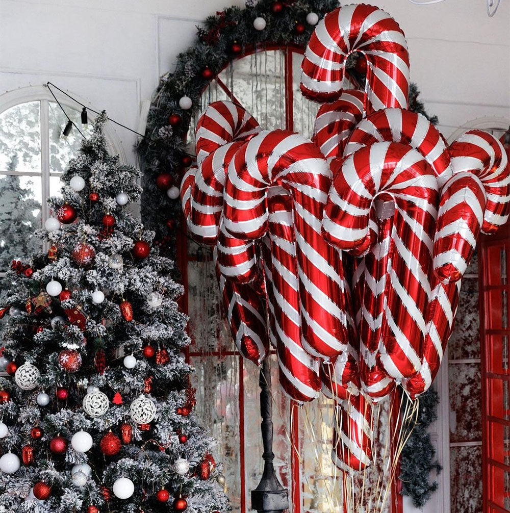 Festive scene with a decorated Christmas tree and a cluster of large red and white candy cane balloons. Snow-covered branches and ornaments accentuate the holiday decor.