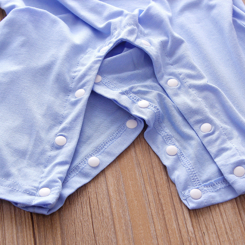 Close-up of a light blue garment with white snap buttons along the seams, lying on a wooden surface. The fabric appears soft, with neat stitching visible around the buttons.