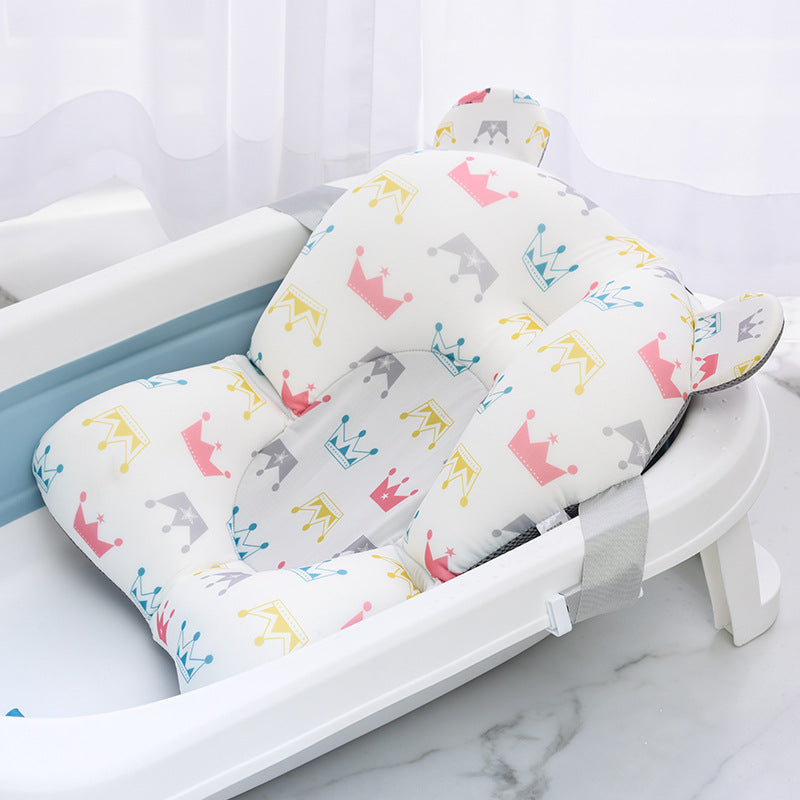 Baby bath seat with colorful crown patterns in pink, yellow, gray, and blue. The seat is placed in a white bath and standing on a marble floor near sheer curtains.