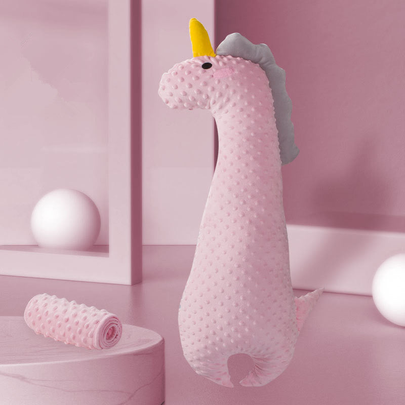 A plush pink unicorn-shaped draft stopper with a yellow horn and gray mane stands on a pink surface, surrounded by pink walls and spherical decor elements.