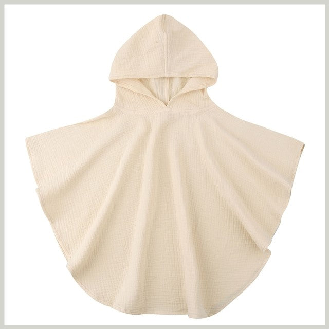 Cream-colored hooded baby towel with a textured fabric, spread out flat. The towel features a rounded shape and open sides, creating a cape-like appearance.