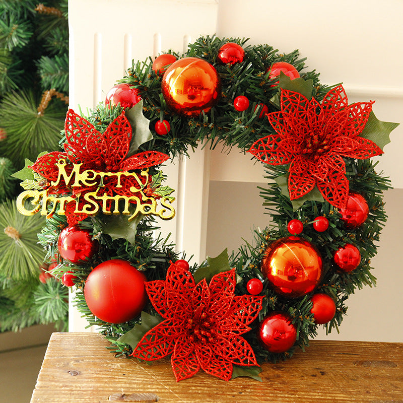 Festive Christmas wreath adorned with red poinsettias, shiny red ornaments, and a golden "Merry Christmas" sign, set against a wooden background with green foliage.