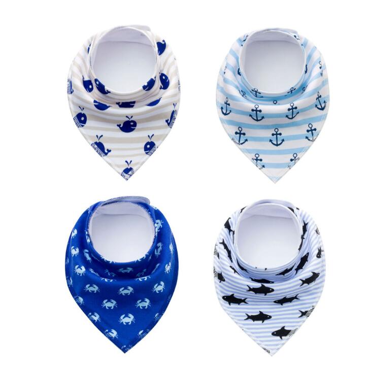Four nautical-themed baby bibs with patterns: whales on cream stripes, anchors on blue stripes, crabs on dark blue, and sharks on gray stripes. All are triangular in shape.
