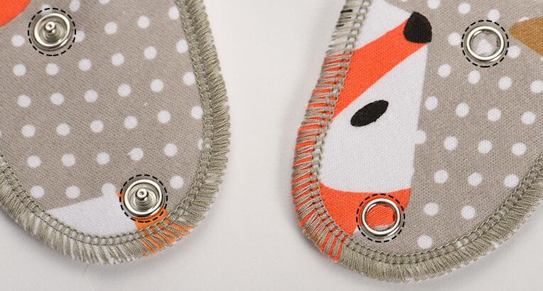 Close-up of two fabric pieces with snap buttons and a gray polka dot pattern. The edges are hemmed with orange and gray threads, displaying a subtle fox design.