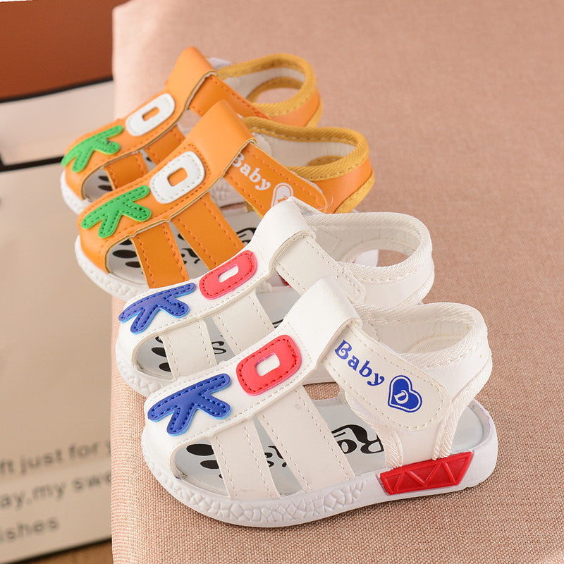 Two pairs of colorful baby sandals on display: one white with blue and red accents, the other orange with green and white designs, both with velcro straps labeled "Baby".