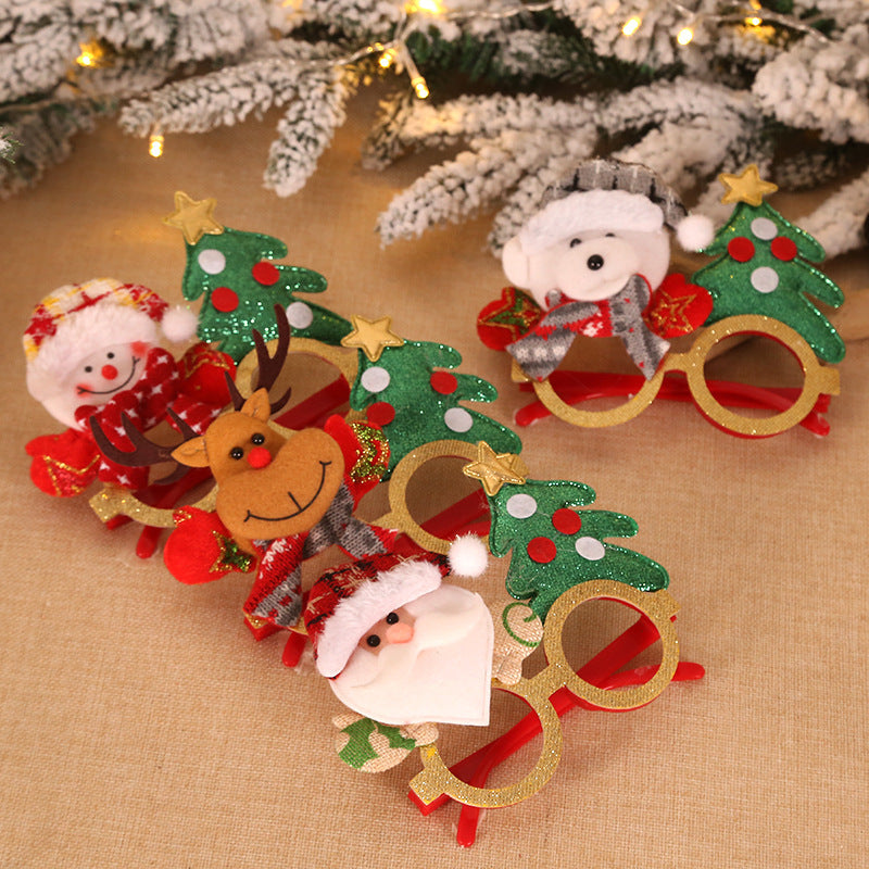 Festive novelty glasses with Christmas tree frames, featuring plush decorations of Santa, a snowman, reindeer, and a bear. Snowy branches with lights are in the background.