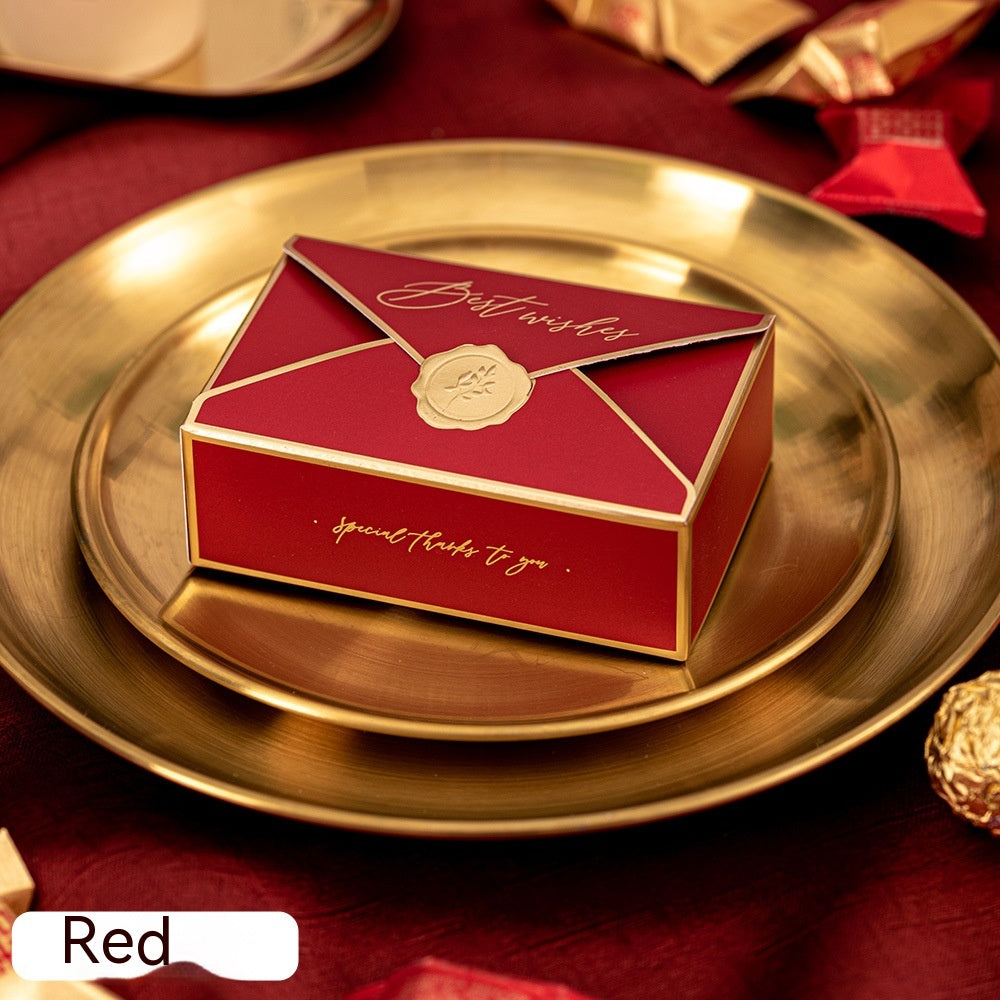 Red gift box resembling an envelope, with gold trim and a seal, sits on a gold plate. The box reads "Best wishes" and "special thanks to you." Decor is elegant and festive.