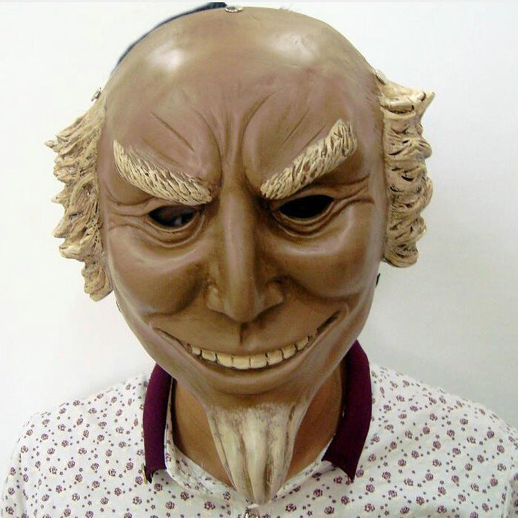 A person wearing a detailed mask with exaggerated features, including bushy eyebrows, a pointed smile, and a goatee. The mask is paired with a patterned shirt.