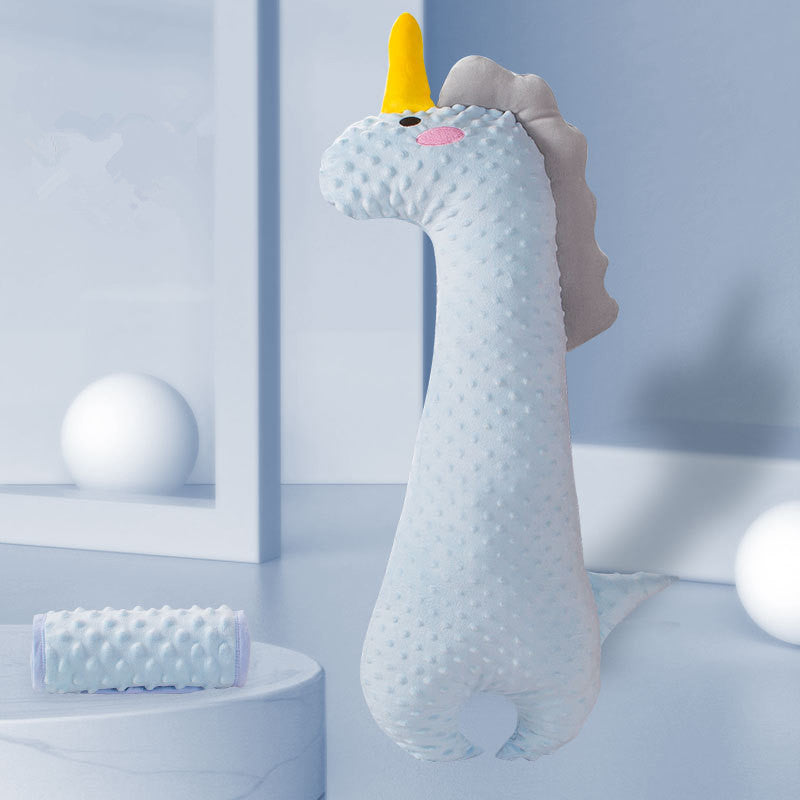 Soft, textured dinosaur toy with a yellow horn and pink cheeks against a light blue background, accompanied by round white objects and a cylindrical pillow.